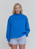 a women wears an electric blue mockneck sweatshirt and striped shorts from the one dna brand