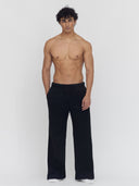 A man on a flat gray background wears black wide-leg sweatpants by One Dna