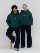 Two people wearing Michigan script hoodies in green