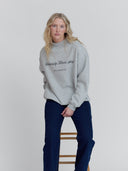 women leans on a stool in heather gray mock neck sweatshirt with minimal script graphic